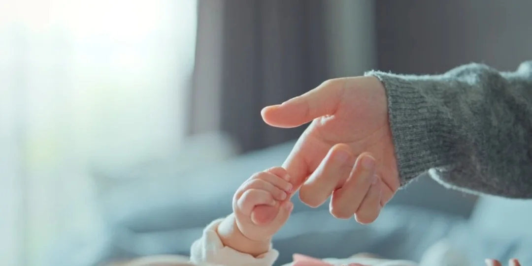 En nyfødt baby som holder mammaen i fingeren