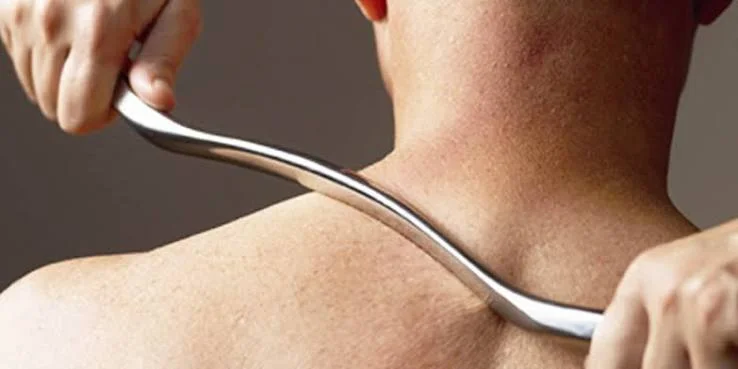 Graston-behandling med et instrument i rustfritt stål langs nakken og skulderen